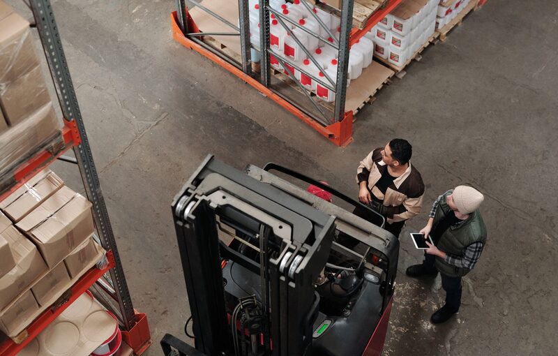 Warehouse staff coordinating stock next to a forklift